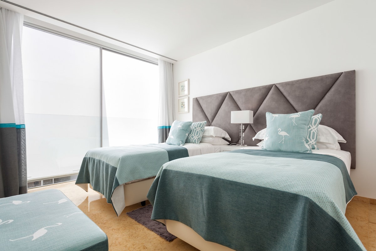 A hotel room with two beds, a large window, and a modern headboard.