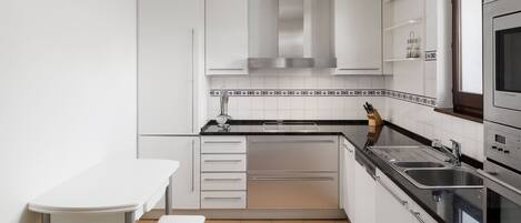 Una cocina compacta con armarios blancos, encimera negra y salpicadero de azulejos.