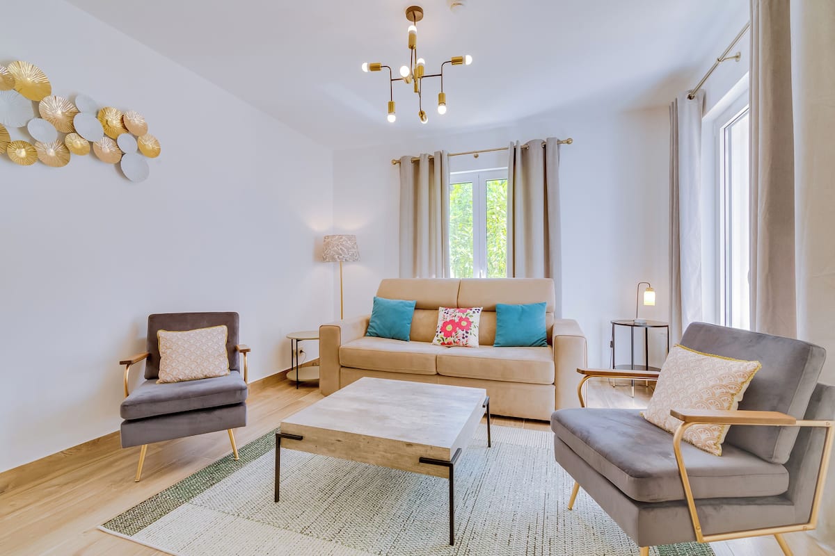 A modern living room with a sofa, two armchairs, a coffee table, and a chandelier.