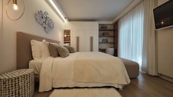 Une chambre moderne avec un grand lit, un pouf rond, un téléviseur fixé au mur et des étagères intégrées.