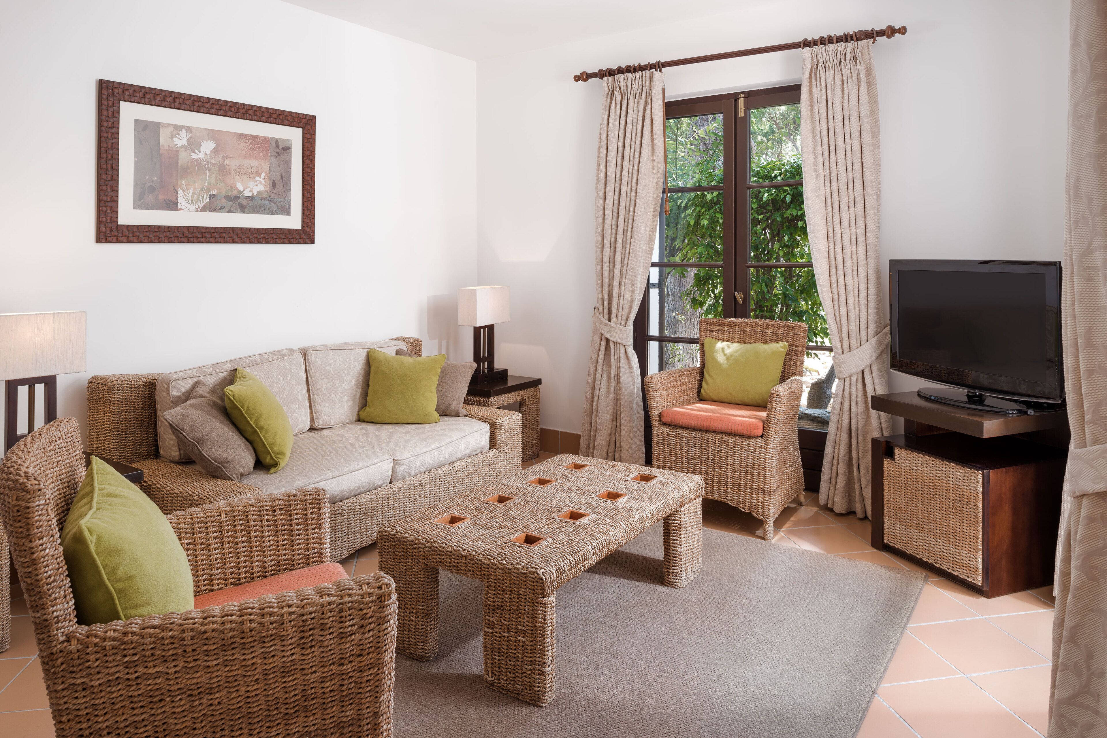 Una sala de estar con sofá, dos sillones, una mesa de centro, televisor y ventana con cortinas.