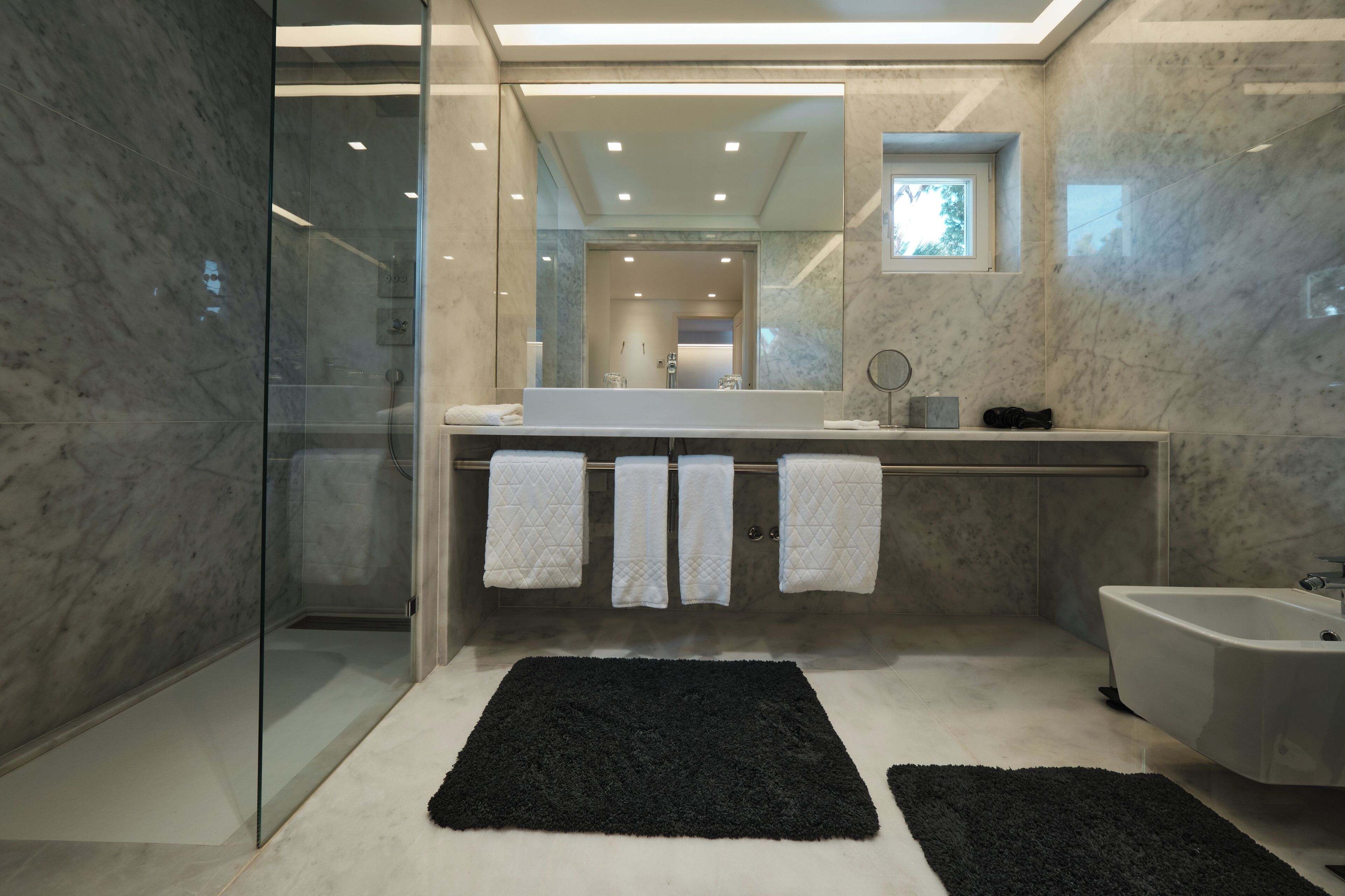 A modern bathroom with a glass shower enclosure, a white bathtub, and a large mirror above the sink.