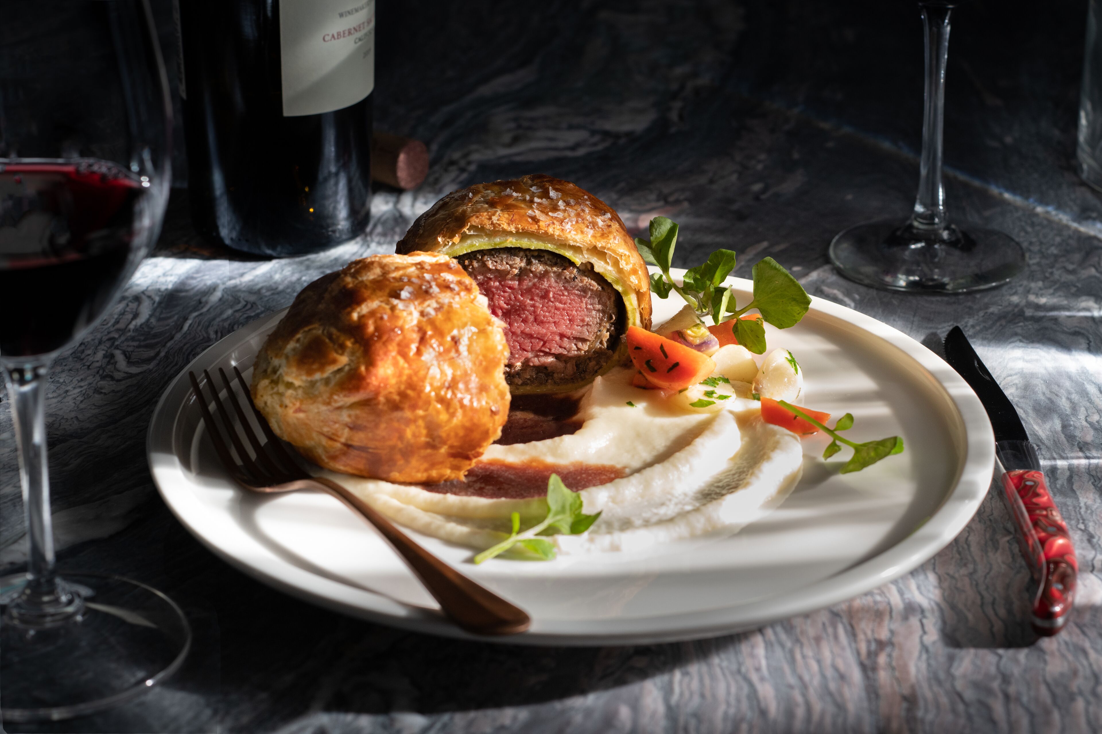 A plate with a beef sandwich and a glass of red wine on a marble table.