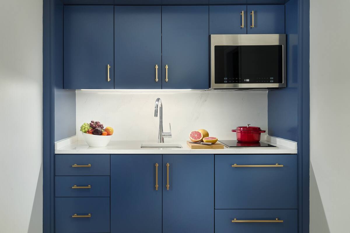 A compact kitchen with blue cabinets, a stainless steel microwave, and a white countertop.