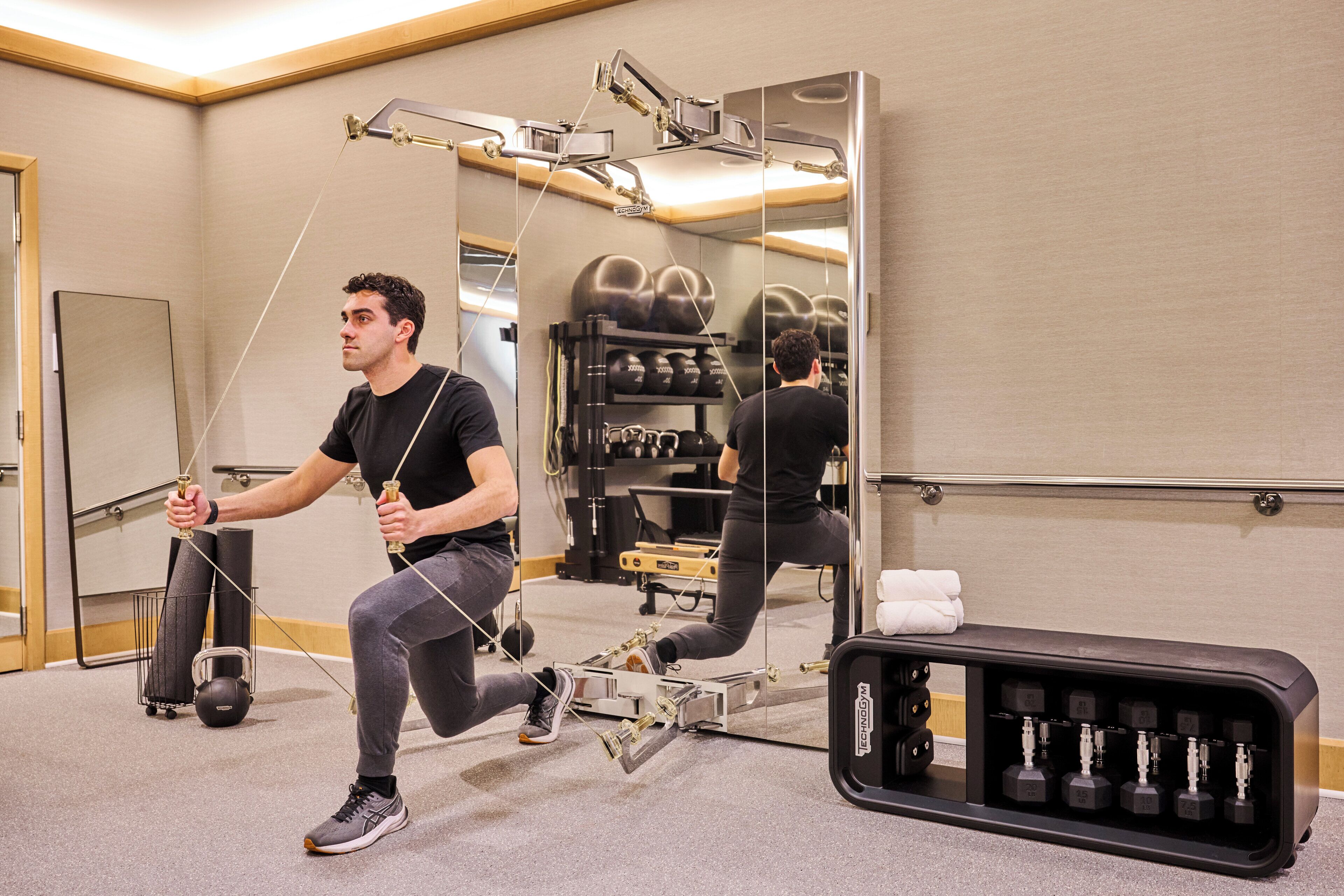 Un homme utilise un appareil de Pilates dans une pièce équipée d’un grand miroir, de ballons d’exercice et d’un porte-poids.