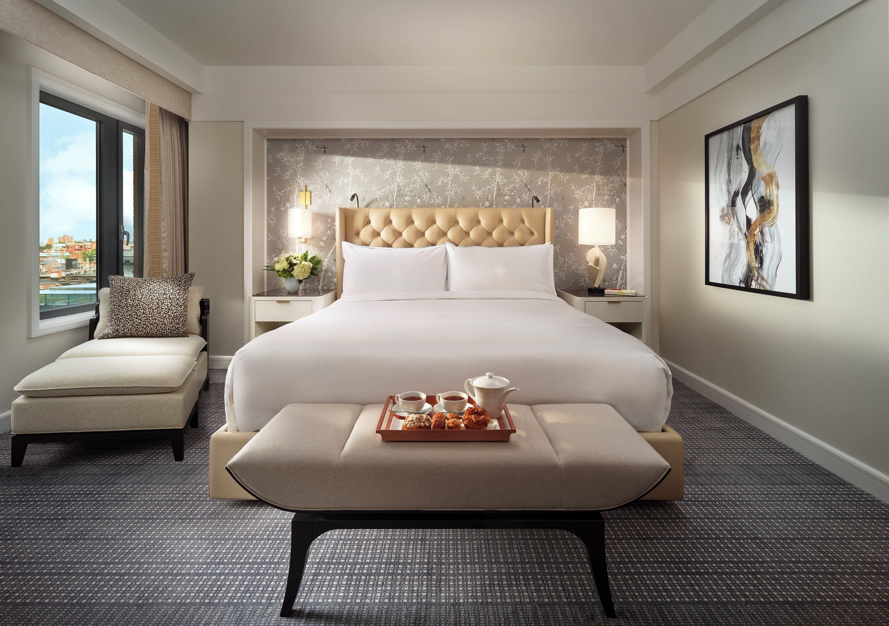 A hotel room with a large bed, a sitting area, a tray with breakfast items, and a city view.