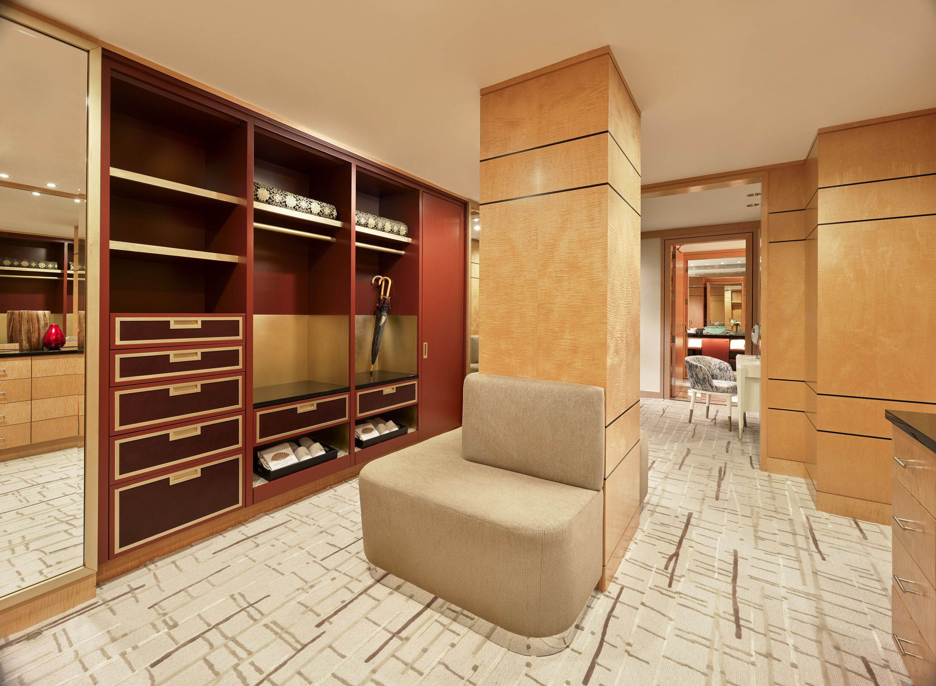 A modern hotel room with a large walk-in closet, a beige armchair, and a patterned floor.