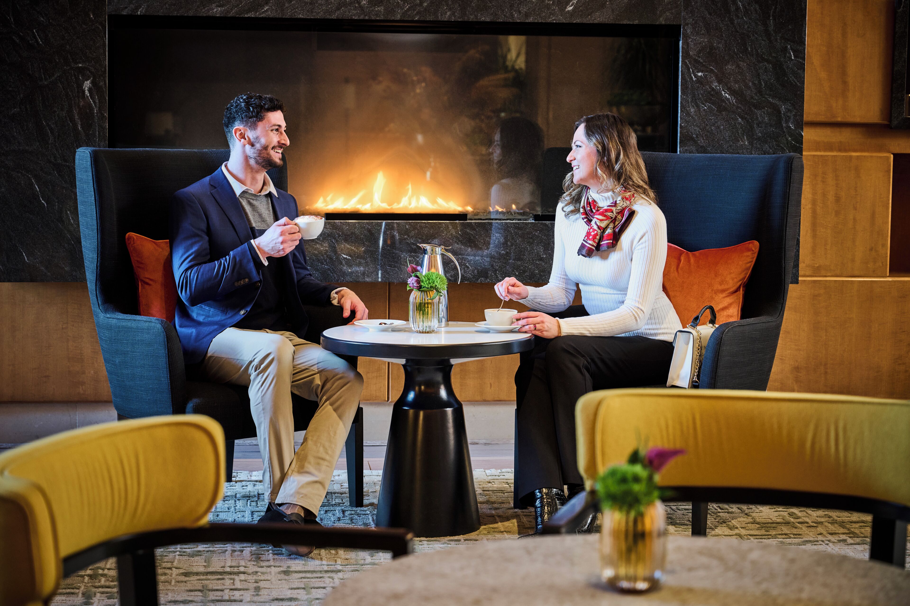 A couple seated at a round table with a fireplace in the background.