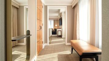 A hotel hallway with a bench, a mirror, and a view into a room with a bed and a desk.