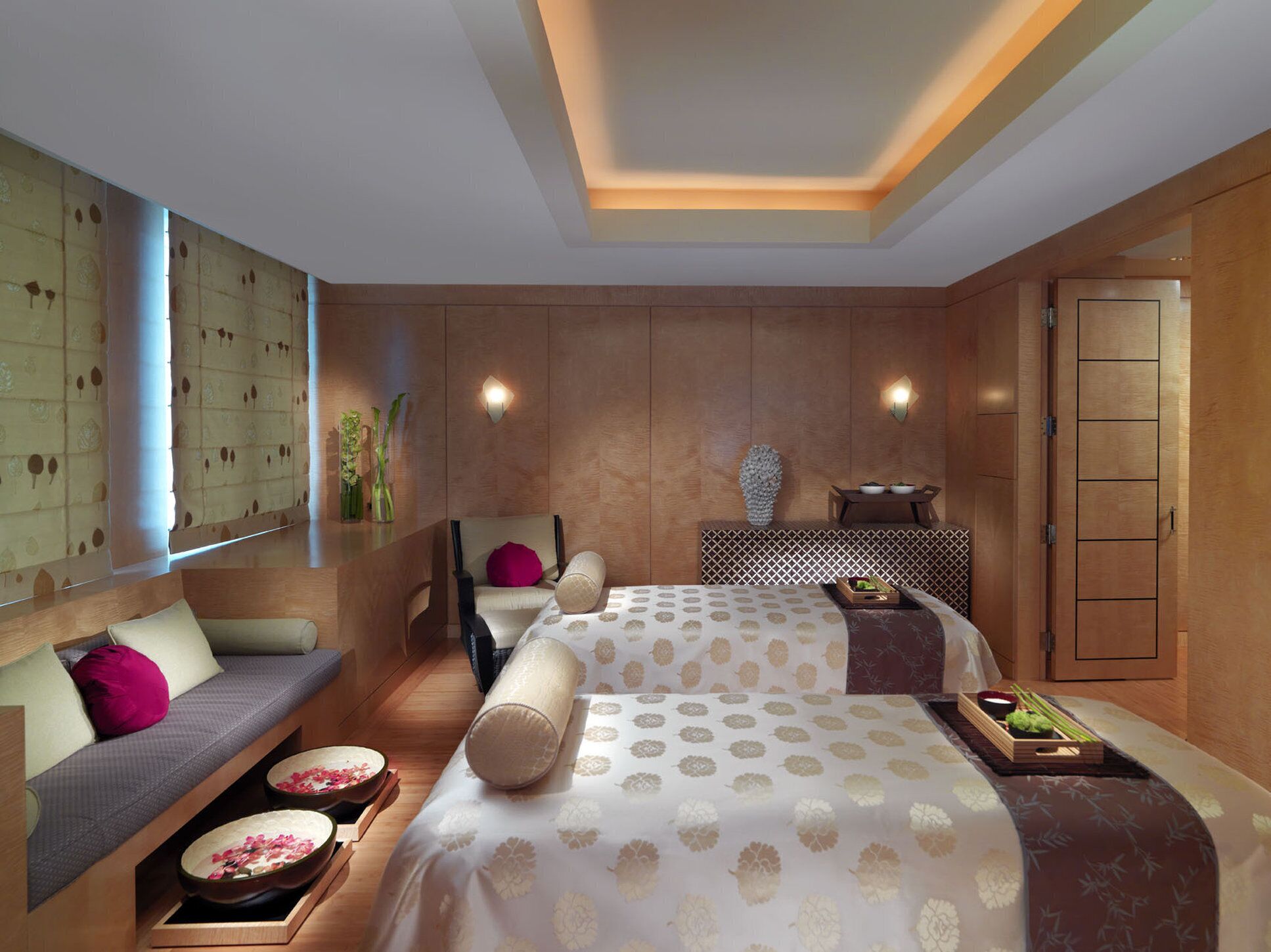 A modern hotel room with a sofa, two beds, a small table, and a decorative wall.