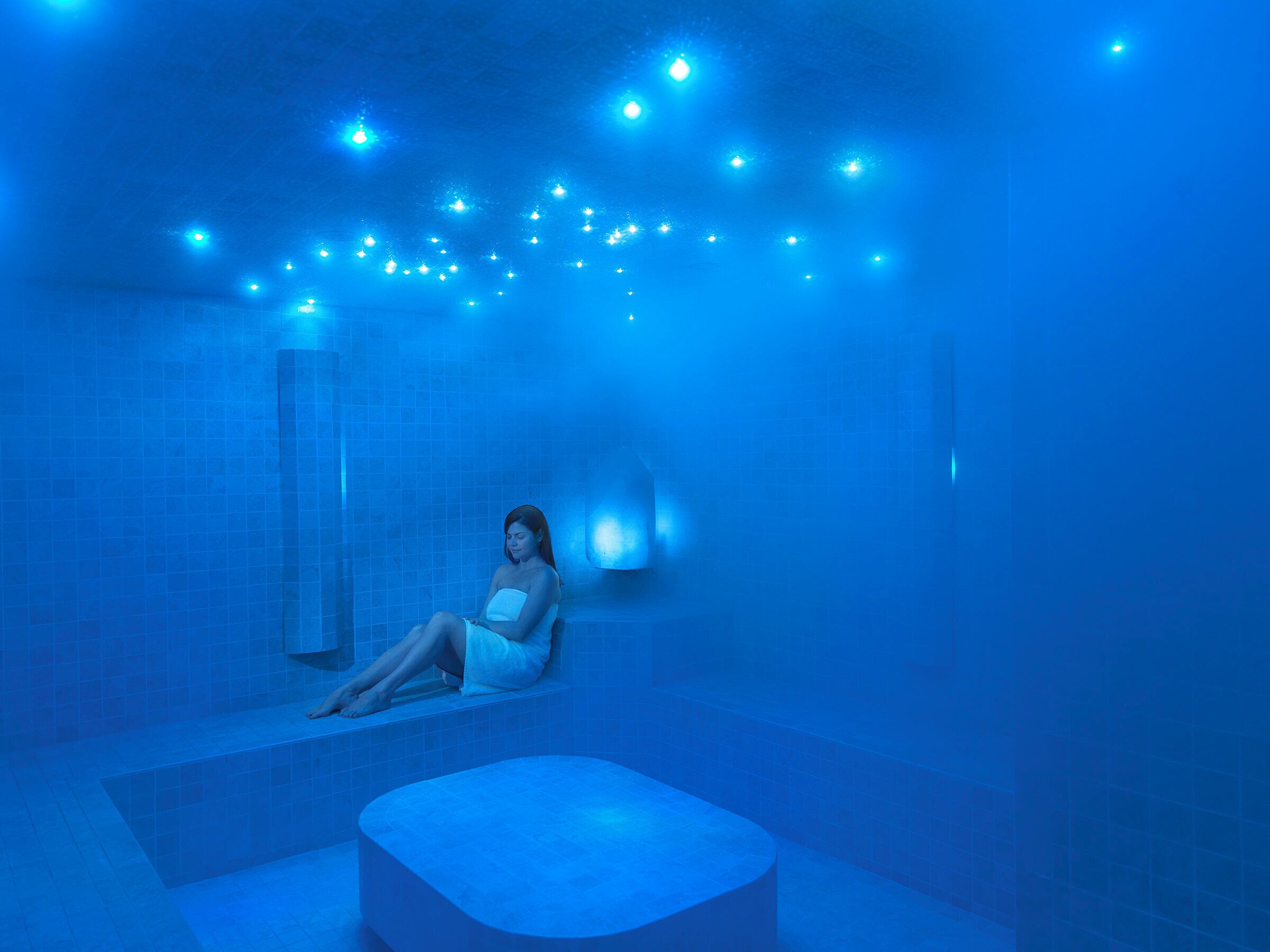 Una persona sentada en una bañera en un ambiente iluminado con luz azul.