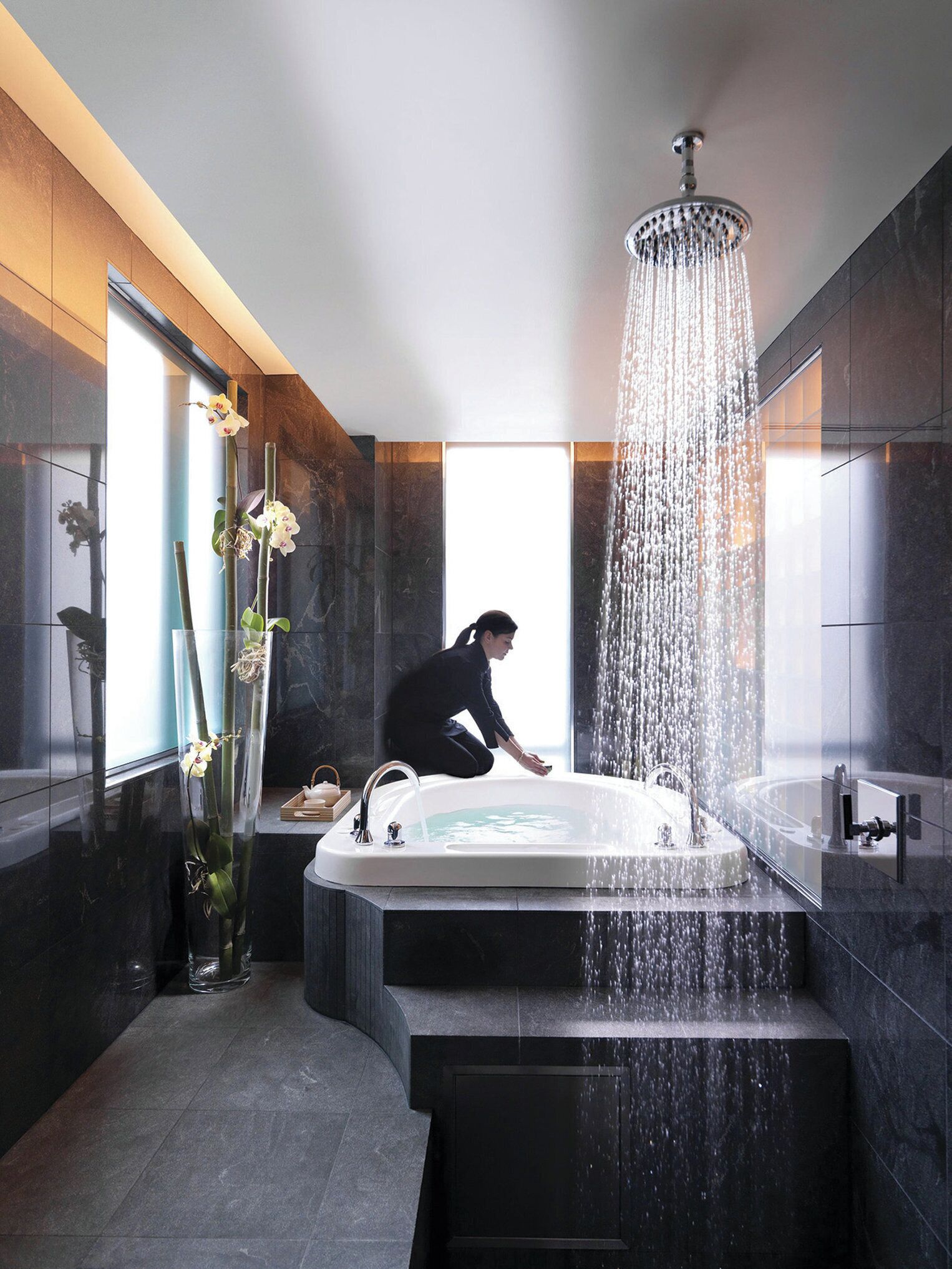 A modern bathroom with a large freestanding bathtub, a showerhead, and a vase with orchids.