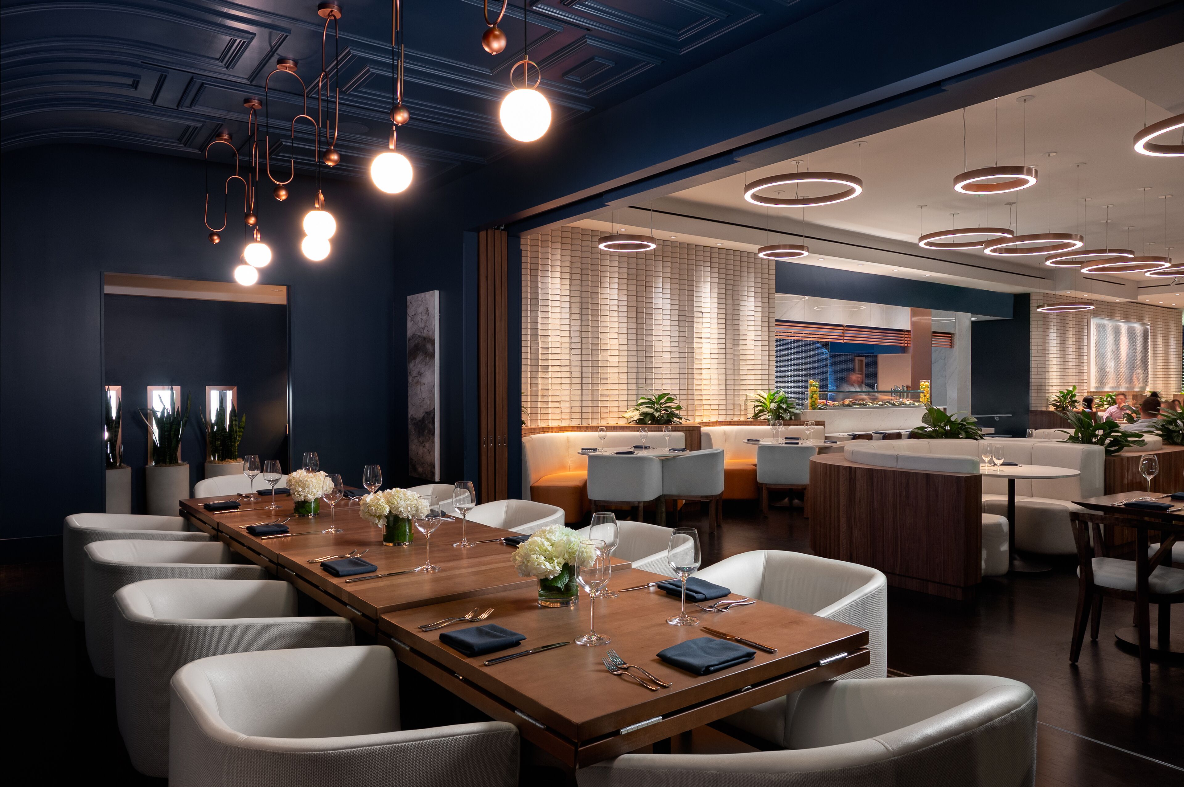 A modern dining area with a long wooden table set for a meal, surrounded by white chairs.