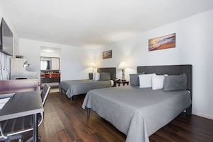 Quarto de hotel com duas camas, uma escrivaninha, uma cadeira, televisão e obras de arte nas paredes.