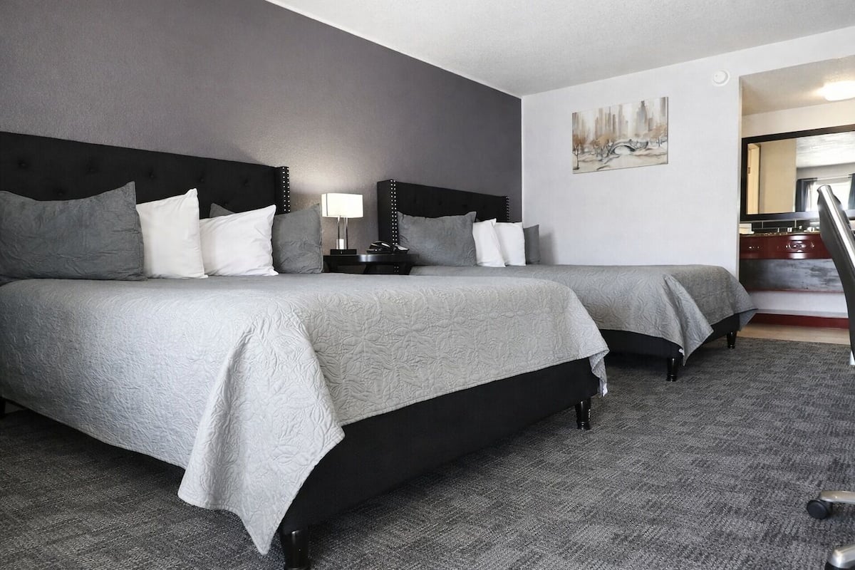 A hotel room with two beds, a nightstand, a lamp, and a painting on the wall.