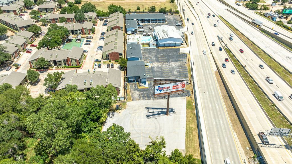 Vista aérea de una zona comercial con varios edificios, un estacionamiento y una autopista.