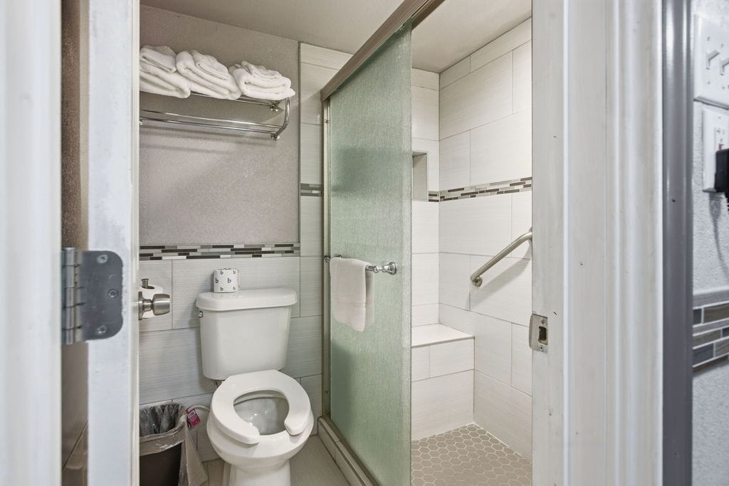 A bathroom with a toilet, a glass shower enclosure, and a towel rack with folded towels.