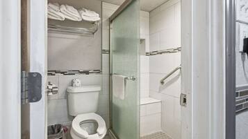 A bathroom with a toilet, a glass shower enclosure, and a towel rack with folded towels.