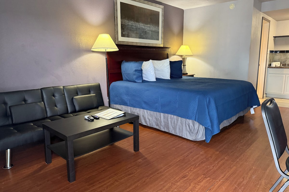 A hotel room with a bed, a sofa, a desk, and two lamps.
