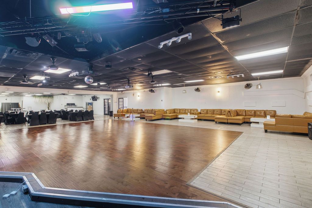 A spacious indoor area with a large wooden floor, multiple seating arrangements, and ceiling-mounted lighting fixtures.