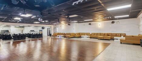 A spacious indoor area with a large wooden floor, multiple seating arrangements, and ceiling-mounted lighting fixtures.