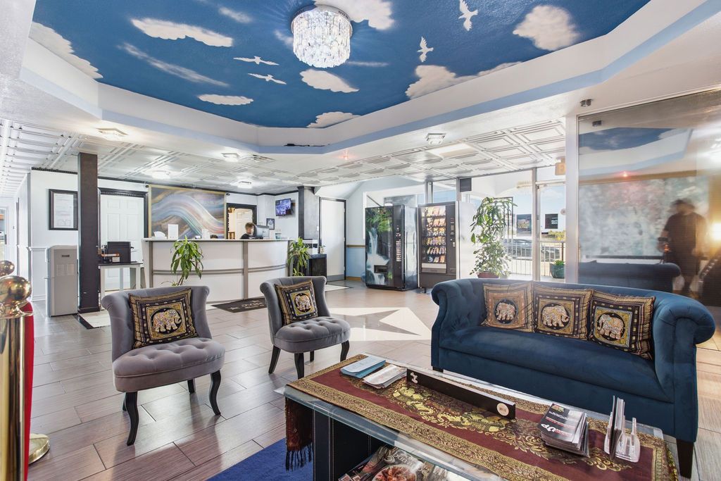 A modern hotel lobby with a high ceiling, a reception desk, seating area, and a chandelier.
