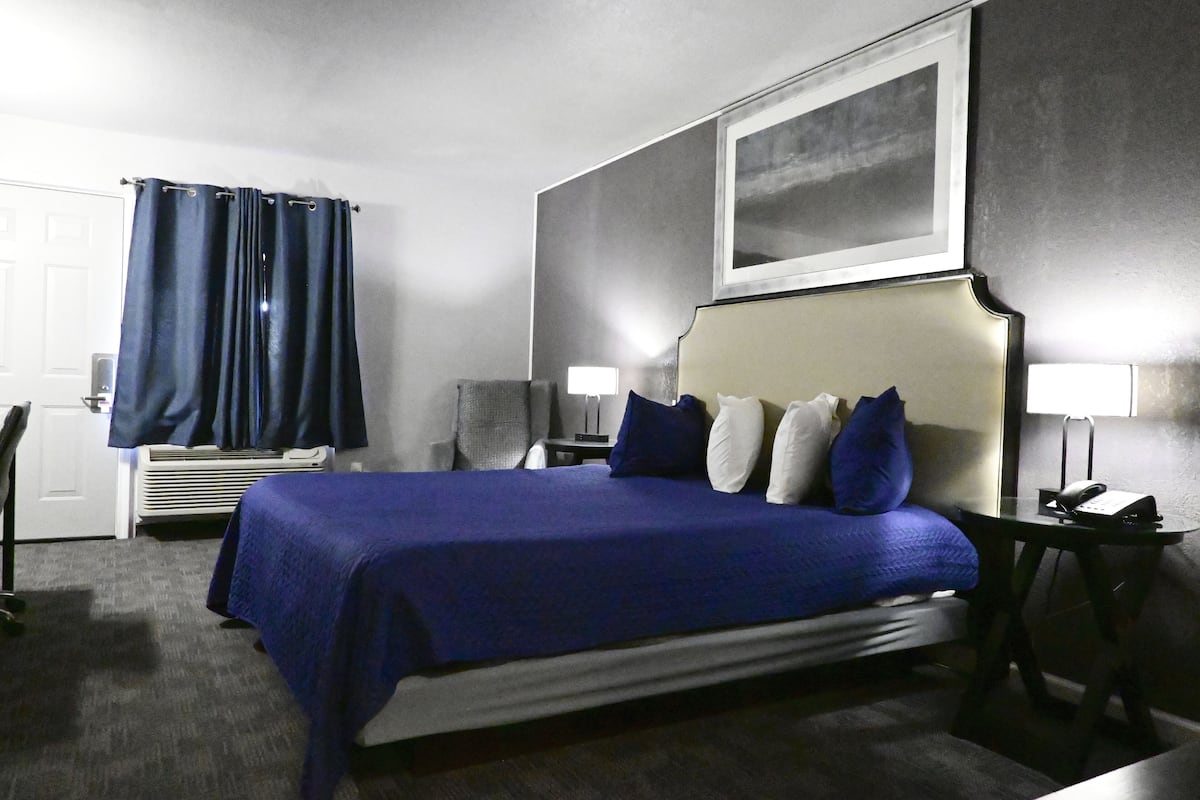 A hotel room with a large bed, a desk, a chair, a lamp, and a telephone.