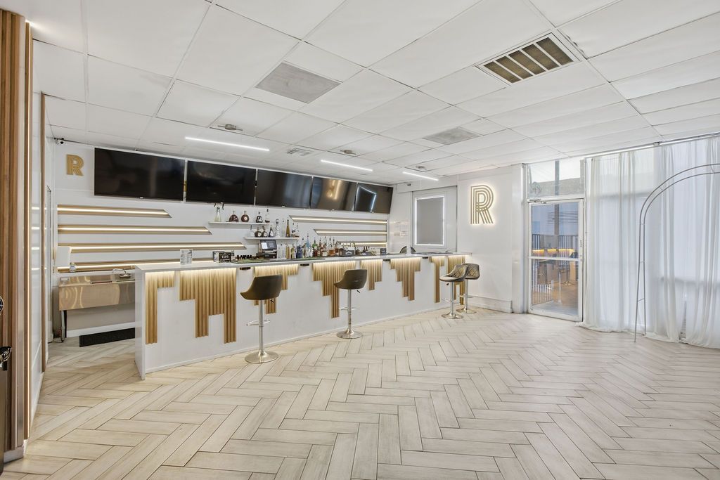A modern bar area with a white countertop, bar stools, and a large window providing natural light.