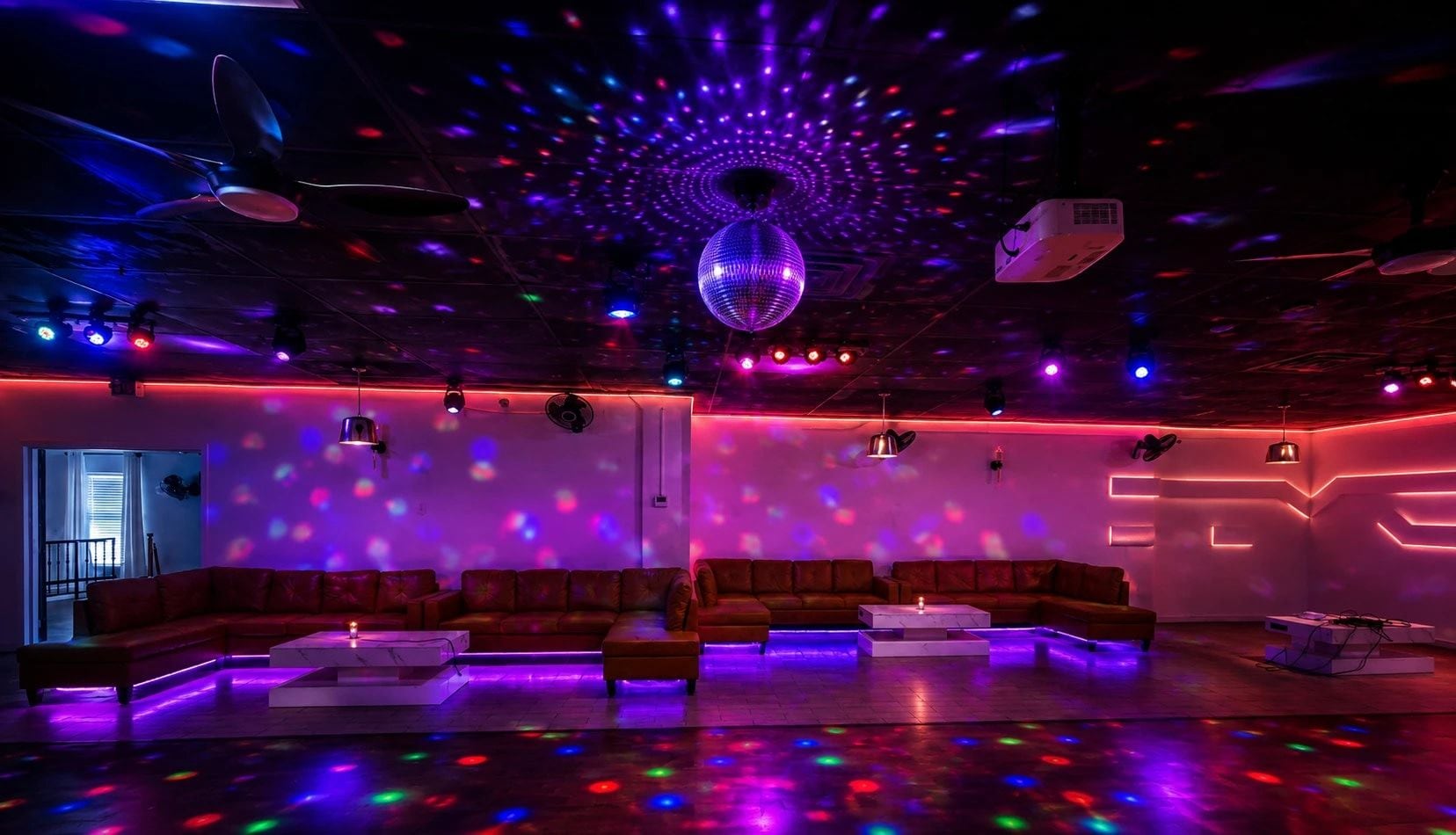 Un área de estar tenuemente iluminada con una bola de discoteca, sofás rojos y una zona de bar.