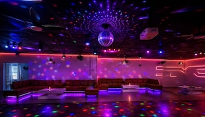 A dimly lit lounge area with a disco ball, red sofas, and a bar area. - R Nite Star Hotel (Arlington)