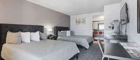 A hotel room with two beds, a desk, a chair, a TV, and a bathroom visible in the background.