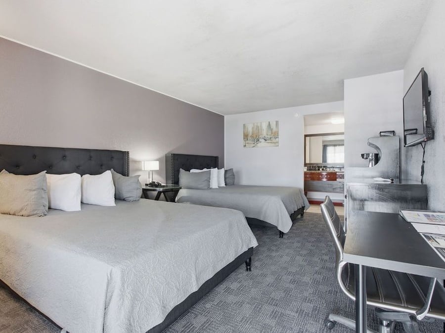 Une chambre d’hôtel avec deux lits, un bureau, une chaise, une télévision et une salle de bain visible au fond.
