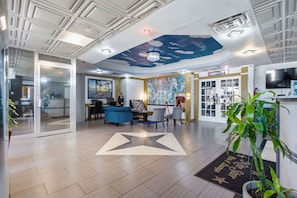 A hotel lobby with a star-shaped carpet, a reception desk, and a wall with a cloud mural. - R Nite Star Hotel (Arlington)