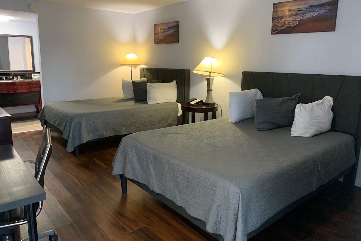 A hotel room with two beds, a desk, and a chair. There are two bedside tables with lamps.