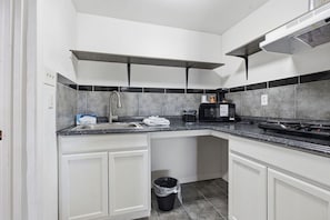 A modern kitchen with white cabinets, a granite countertop, a stainless steel range hood, a microwave, and a trash can. - R Nite Star Hotel (Arlington)