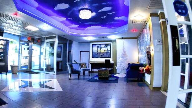 Een moderne lobby met een plafond waarop een hemel en wolkenschildering is aangebracht, een receptiebalie, een zithoek met stoelen, en een groot raam met uitzicht.