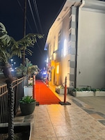 Vista noturna de uma rua com um tapete vermelho que leva a um edifício de fachada branca e várias janelas.