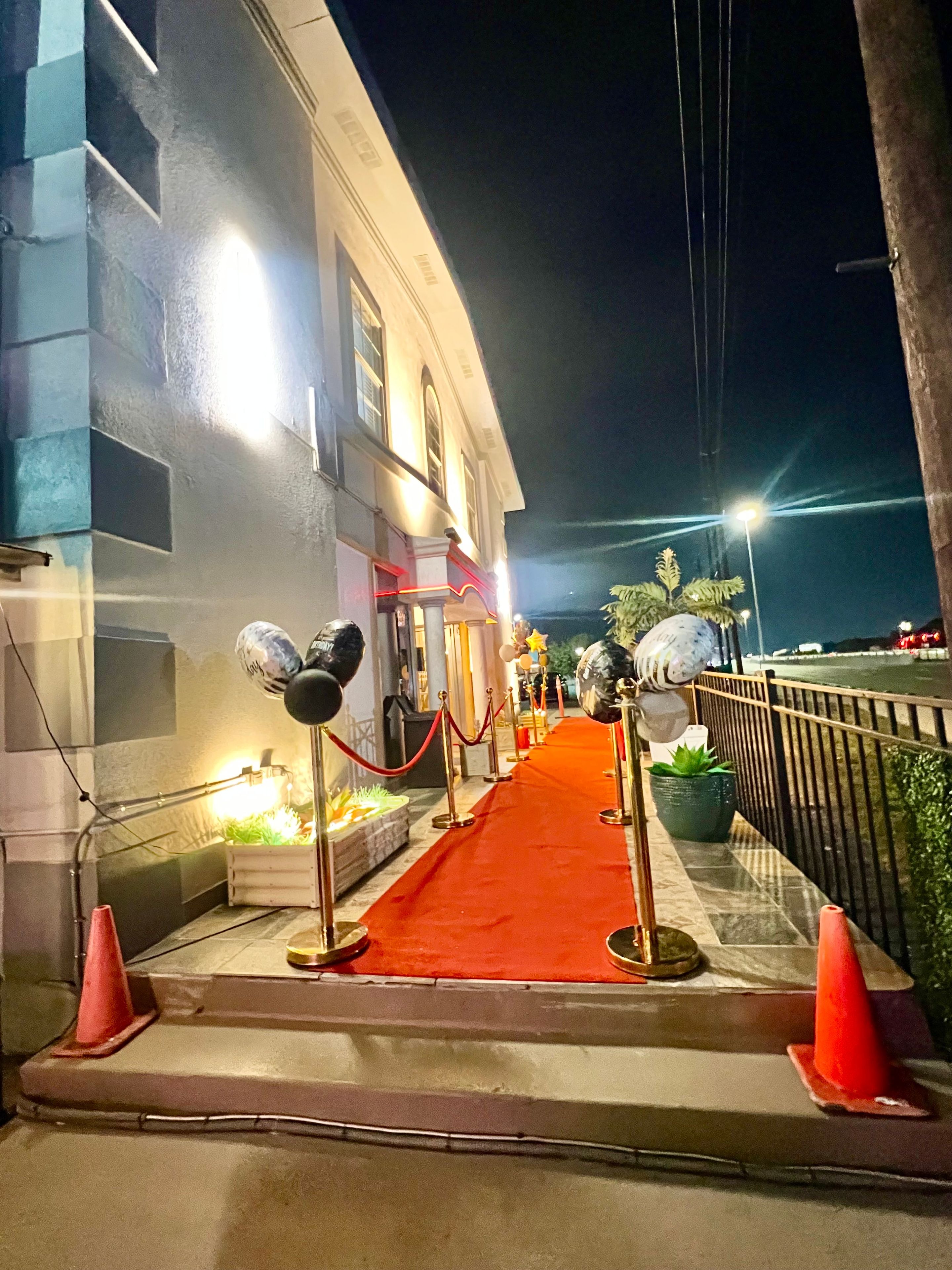 Un tapis rouge menant à l’entrée d’un bâtiment, avec une barrière de sécurité et une corde rouge.