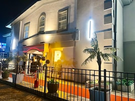 Fachada de hotel com um grande letreiro em formato de 'P', entrada com portão e vasos de plantas.