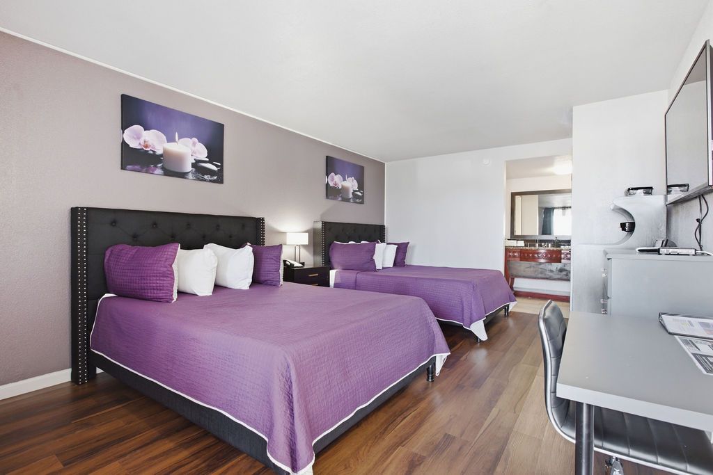 Una habitación de hotel con dos camas, un escritorio y un baño visible al fondo.