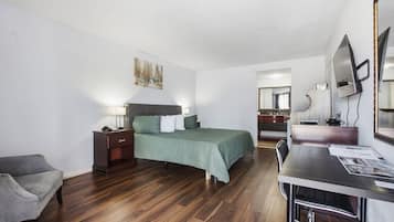 Ein Hotelzimmer mit Bett, Schreibtisch, Stuhl, Kommode und Spiegel.