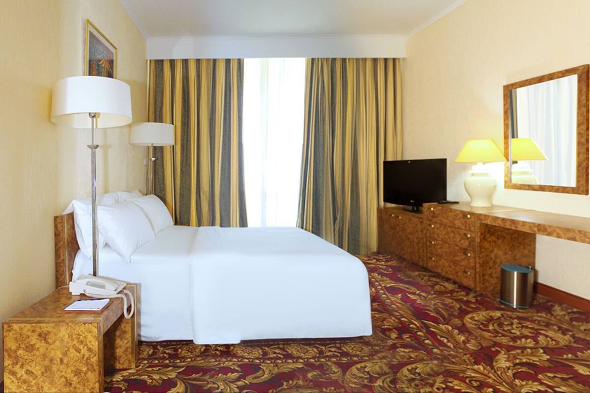 A hotel room with a bed, a desk with a telephone, a television, and a mirror.