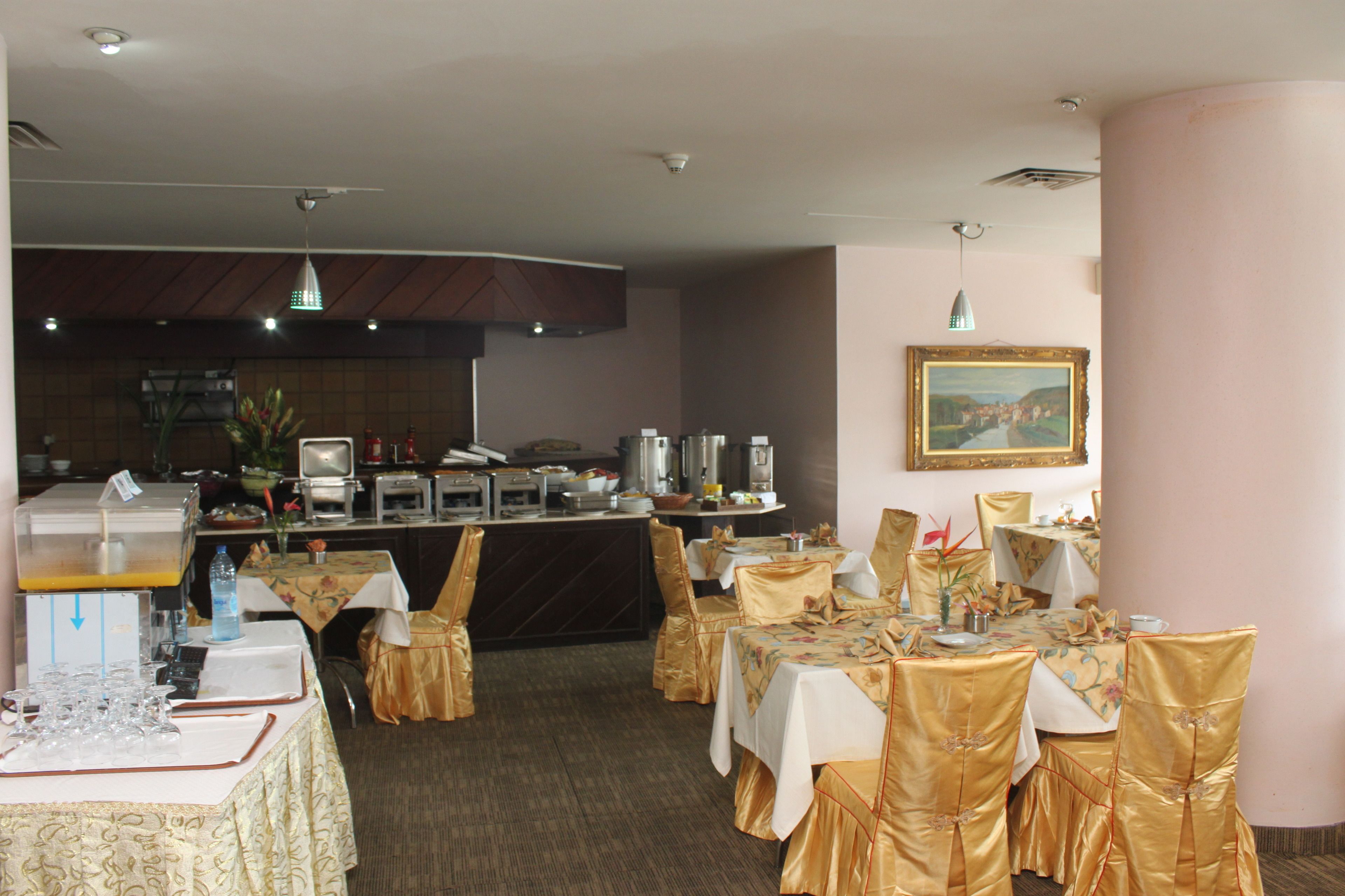 A restaurant with tables set for dining, a bar area with a counter, and a painting on the wall.