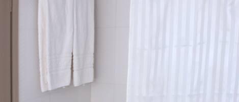 A bathroom with a bathtub, a shower curtain, and two white towels hanging on the wall.