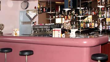 Een bar met een roze toonbank, krukken en planken vol verschillende flessen.