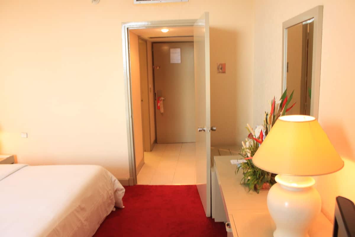 A hotel room with a bed, a red carpet, a lamp, and a door leading to another room.