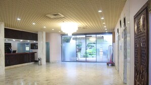 Eine geräumige Lobby mit Marmorboden, einer Rezeption und einer großen Glastür zum Außenbereich.
