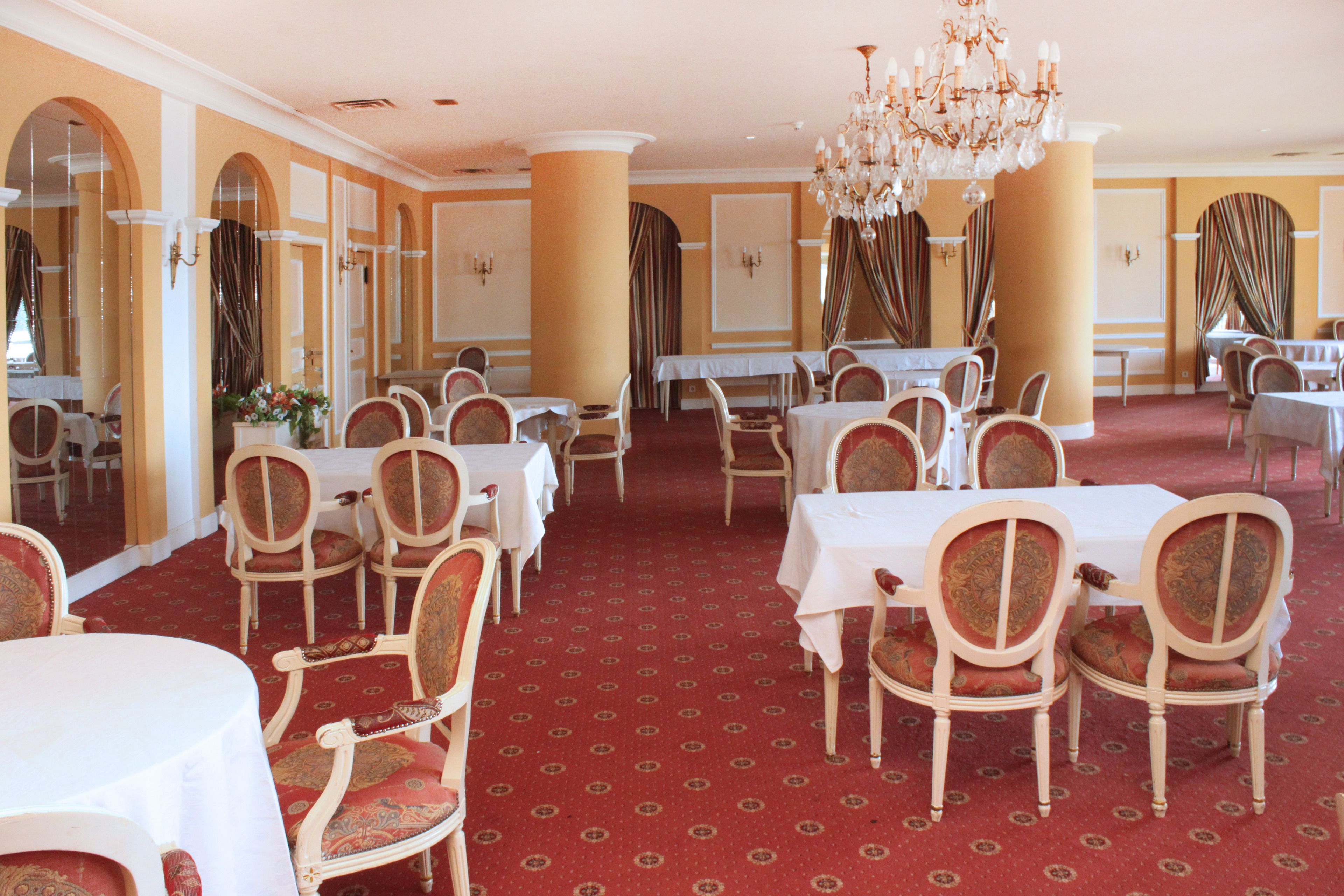 Un comedor formal con varias mesas y sillas, una alfombra estampada y una araña.