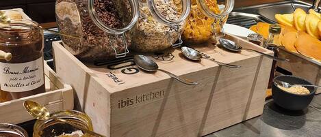 A buffet setup with various food items and condiments, including jars of spreads and a bowl of cereal.