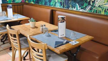 Un restaurant avec des tables et des chaises en bois, un présentoir à menus et un mur décoratif.